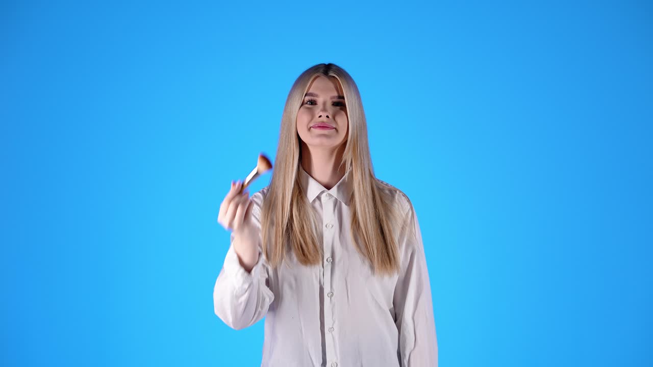 una joven segura se aplica polvo con un pincel cosmético, fotografía de estudio, azul