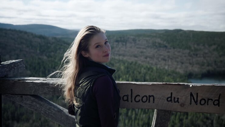 Chica joven encantadora de pie en una plataforma de observación de madera, posando para una foto con un lago forestal de fondo en Saint-Come, Quebec, Canadá.