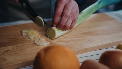 una persona corta un puerro en una tabla de cortar de madera con naranjas frescas cerca