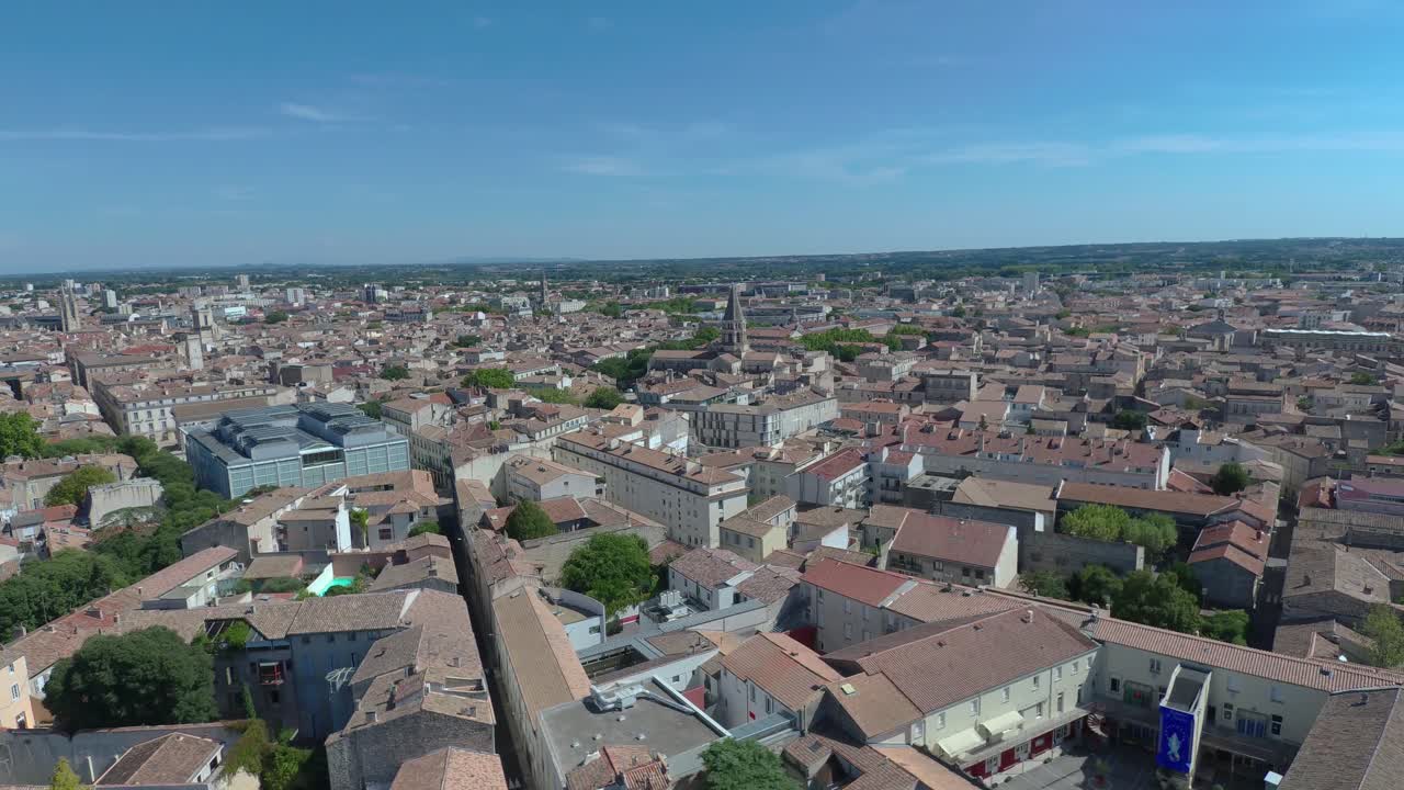 Ripresa aerea con drone sopra Nîmes che rivela un denso paesaggio urbano sotto un cielo azzurro limpido