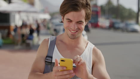 Retrato-De-Un-Joven-Atractivo-Que-Utiliza-Mensajes-De-Navegación-Por-Teléfono-Inteligente-Enviando-Mensajes-De-Texto-En-Línea-Disfrutando-De-La-Comunicación-Móvil-En-Viajes-Turísticos-Urbanos-Cálidos-Y-Soleados-Frente-A-La-Playa