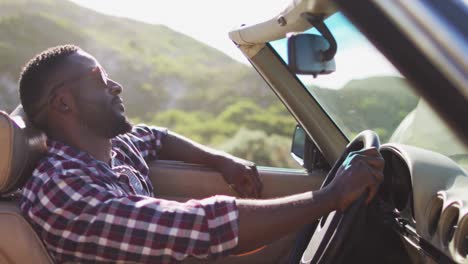 African-american-man-with-hands-on-steering-wheel-sitting-in-the-convertible-car-on-road