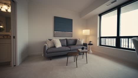 push in shot of a cozy den area in a home with a grey couch and large windows letting in natural light