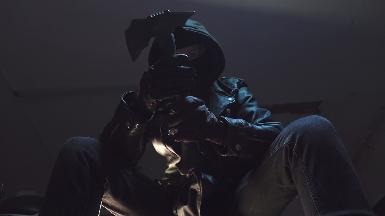 Kriminel med banditmaske og sorte læderhandsker kigger på en økse og tester dens vægt.