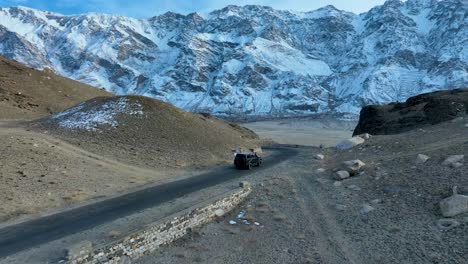 Vista-Aérea-De-Un-Todoterreno-Que-Atraviesa-Una-Carretera-Sinuosa-En-Medio-De-Un-Paisaje-Montañoso-Nevado,-Mostrando-Una-Sensación-De-Aventura-Y-Aislamiento.