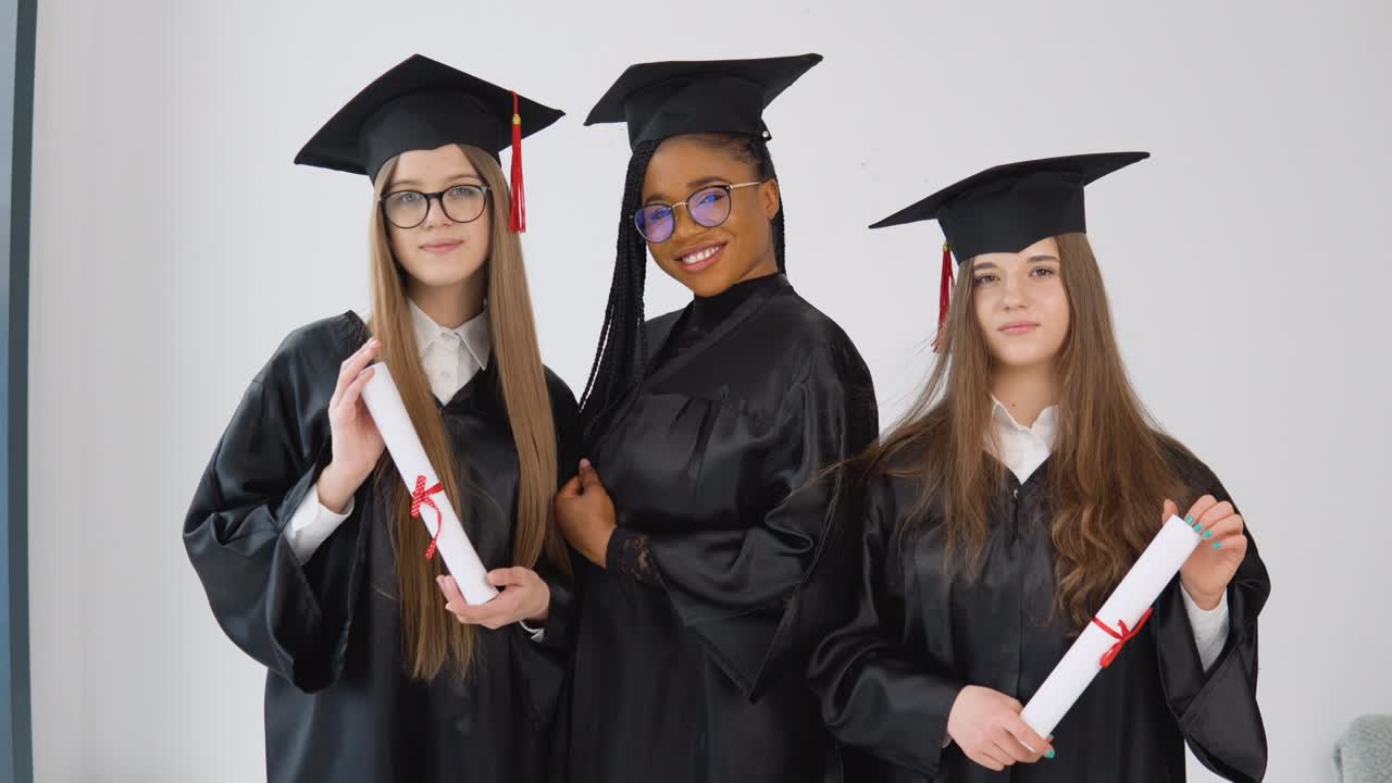 tres jóvenes graduadas felices de diferentes nacionalidades están juntas uno al lado del otro con diplomas en las manos. vista de cerca sobre fondo blanco