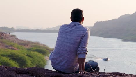 isolated-young-man-sitting-at-mountain-top-with-lake-view-from-flat-angle-video-is-taken-at-kaylana-lake-jodhpur-rajasthan-india