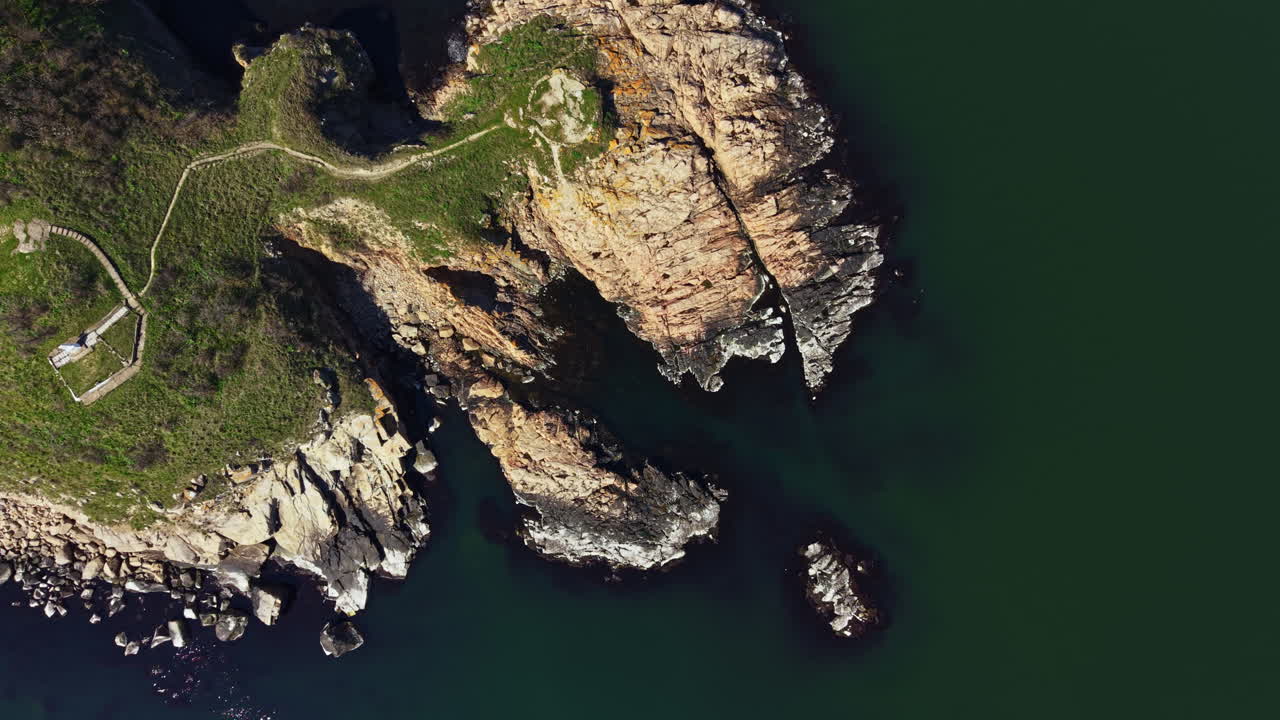 Costa rocciosa con sentieri verdi durante una giornata di sole vicino all'acqua, in un ambiente esterno con chiara visibilità di rocce e mare.