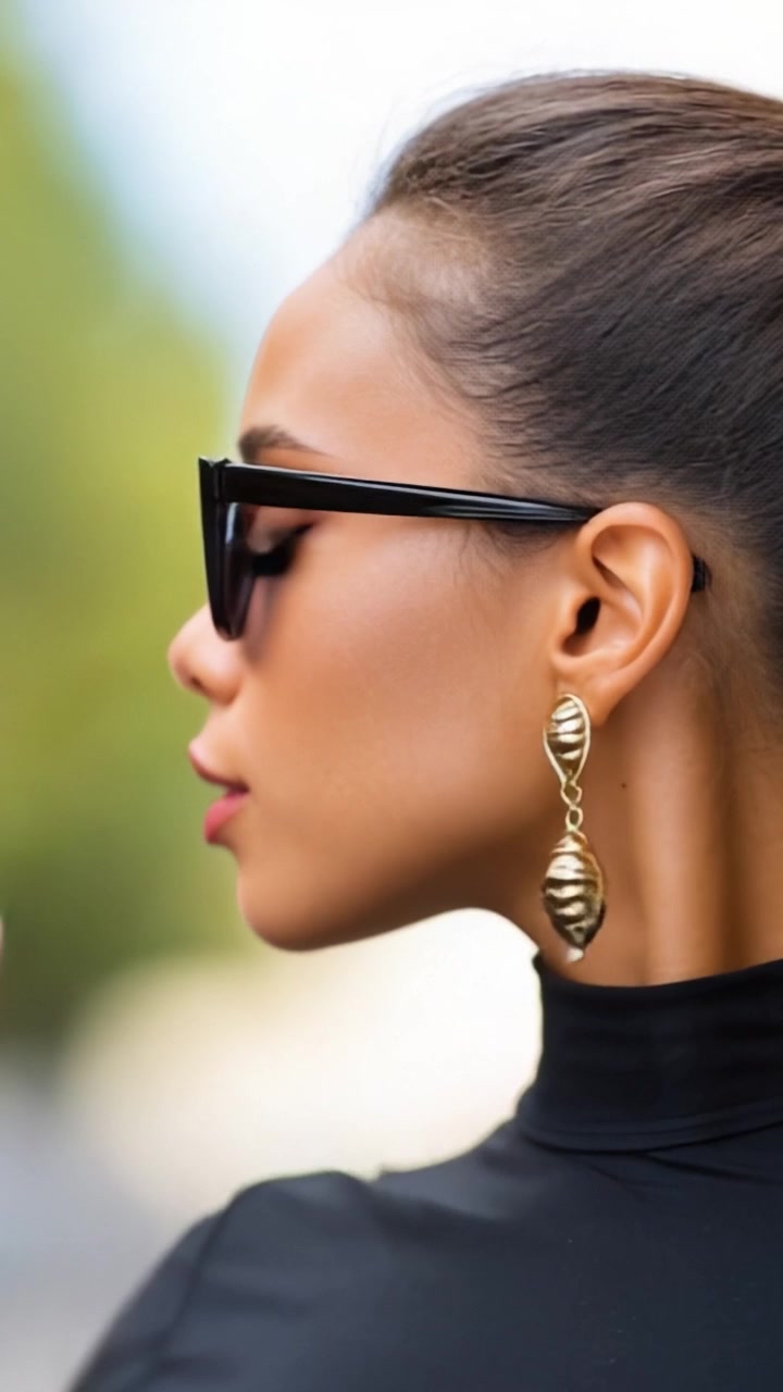 Donna sofisticata con occhiali da sole a occhi di gatto e orecchini eleganti in un ambiente esterno glamour, che sfoggia moda e stile in un'atmosfera urbana.