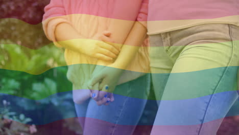 animation of rainbow flag over diverse female couple holding hands