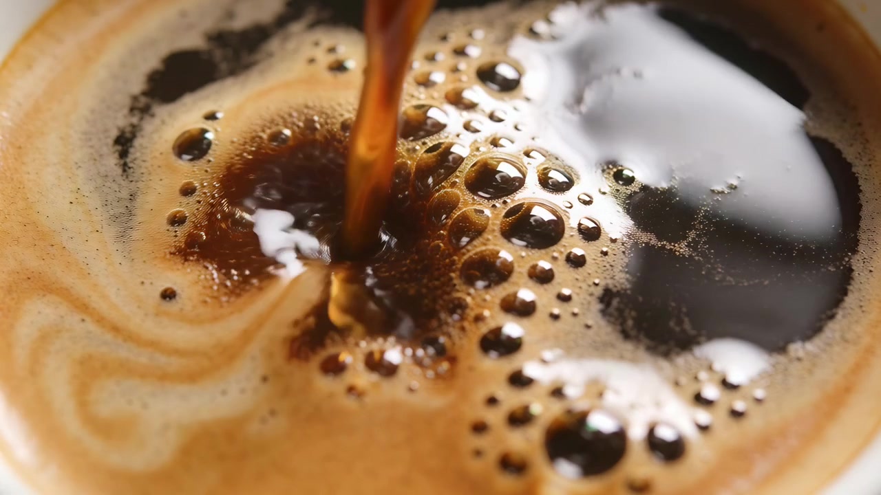 Espressostråle hælder ned i en keramisk kaffekop for at fylde koppen, kaffeoverfladen danner crema og bobler