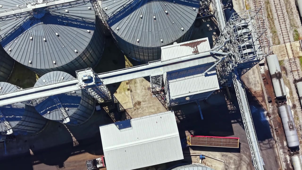 Storage tanks are lined up and organized at a grain facility in a rural area during daylight hours
