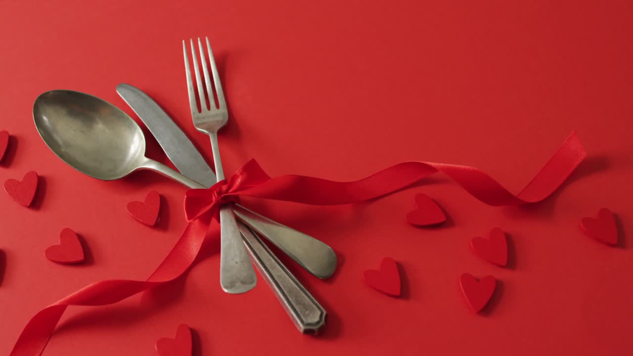 Red ribbon and cutlery with hearts on red background at valentine's day