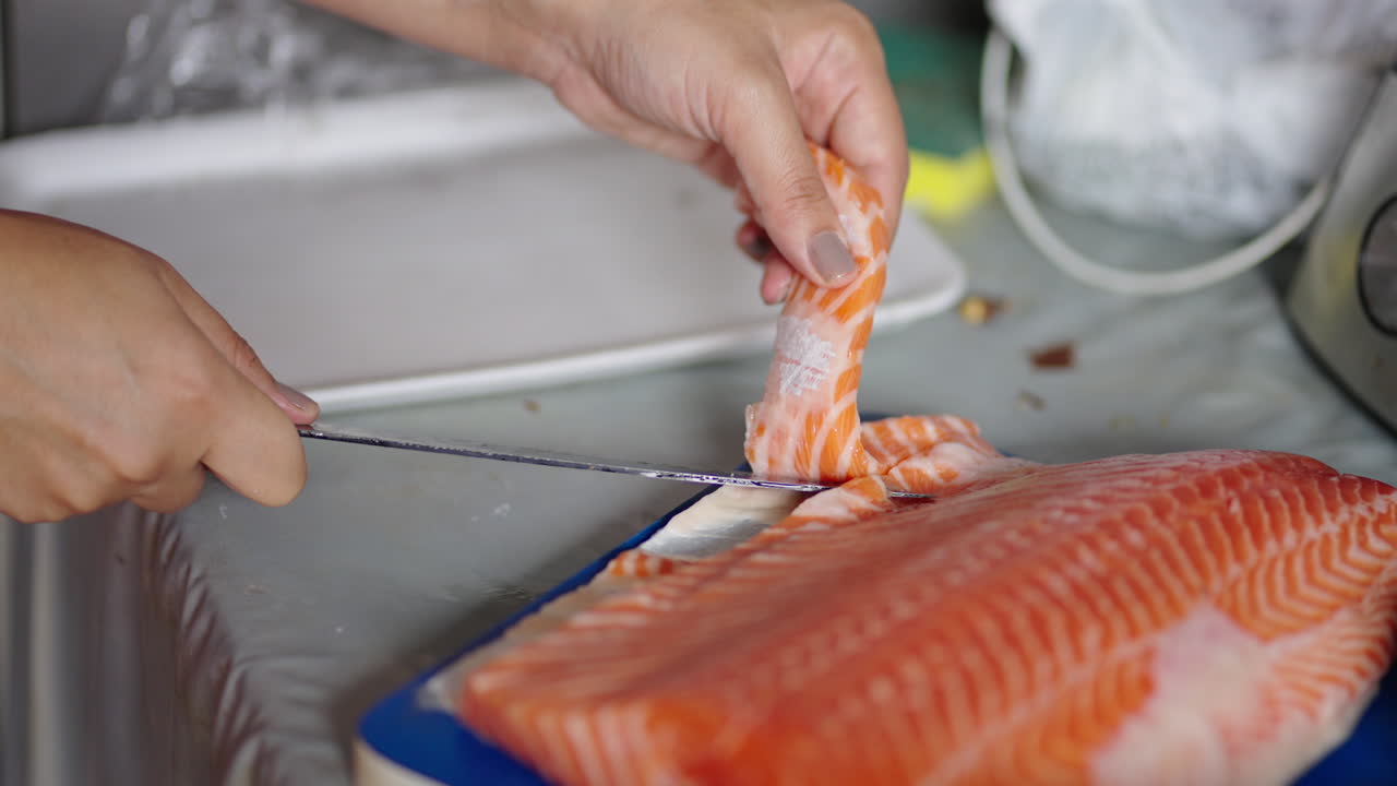 Slicing fresh raw salmon by hand with knife for sashimi preparation. Close-up