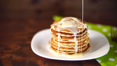 condenced milk being poured on a stack of pancakes.