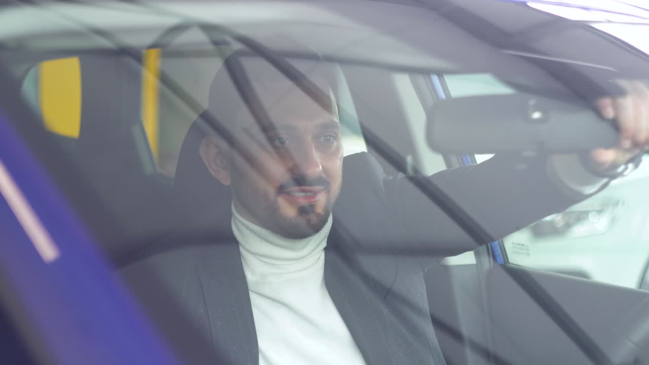 Bearded man looks in the rearview mirror in the car. Side view. Auto business, car sale, technology and people concept