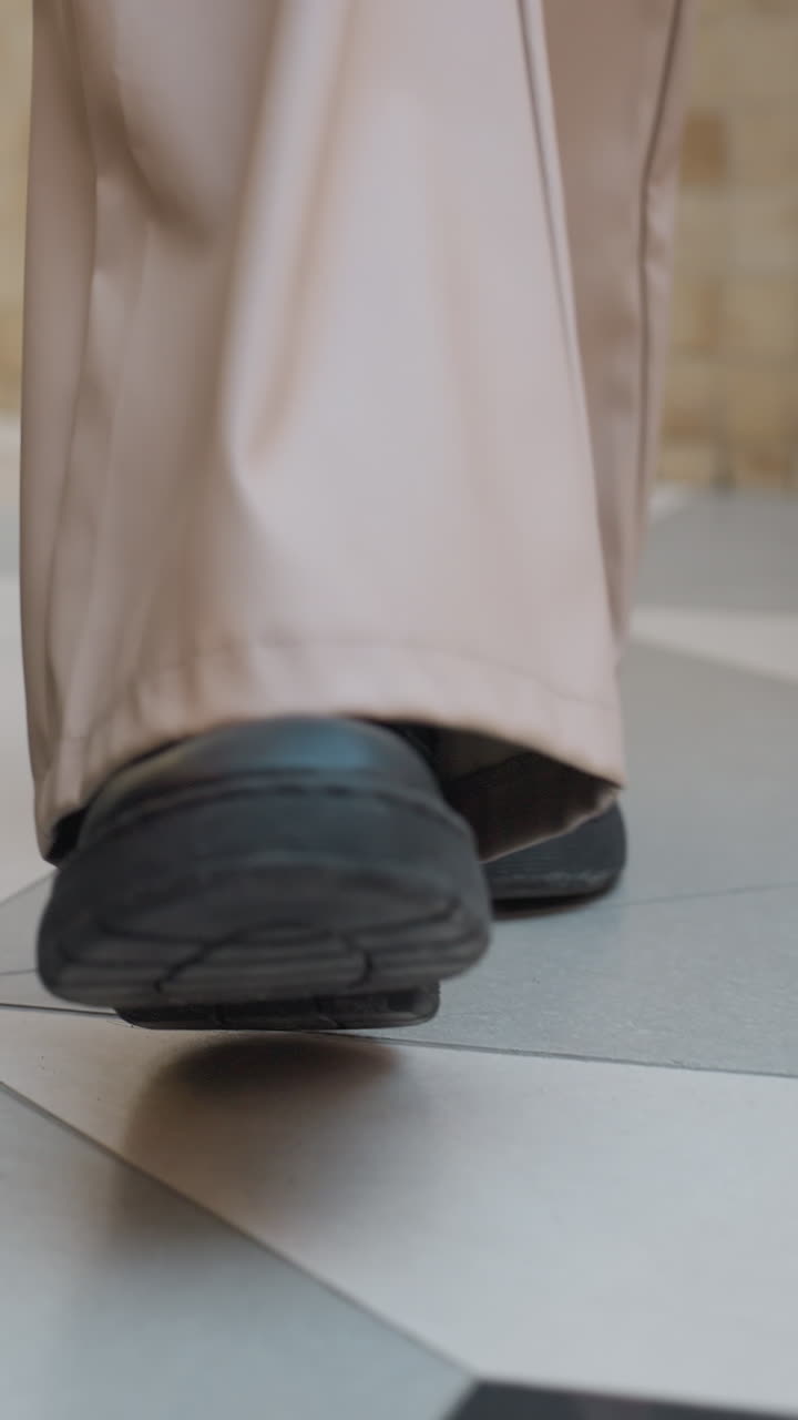 Lower angle view of woman in large trousers and black shoes walking towards Christmas tree in a shopping mall with festive decorations