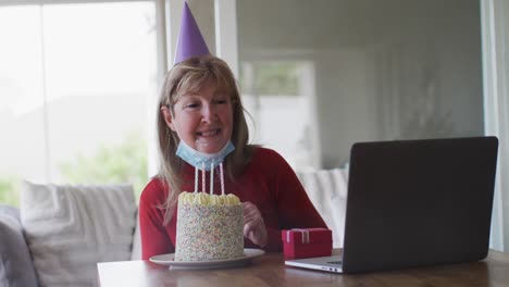 senior woman blowing cake while having a video chat on laptop at home