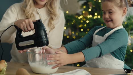 caucasian mother and daughter preparing baking using electric mixer in the kitchen before christmas.