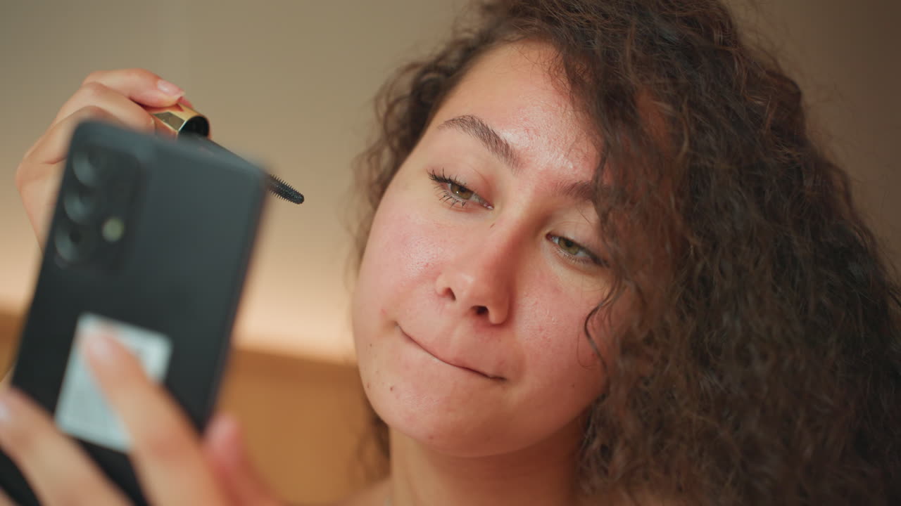 Woman prepares makeup. Woman in hotel room using smartphone as mirror for makeup preparation. Female individual in accommodations utilizing handheld device as mirror for cosmetic application