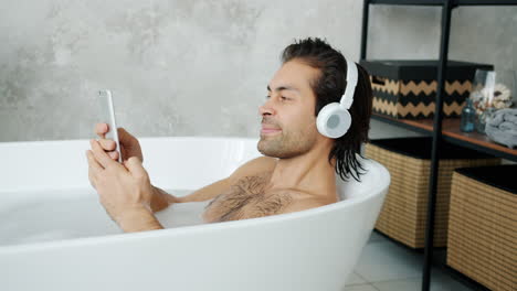 man relaxing in a bubble bath with headphones and tablet
