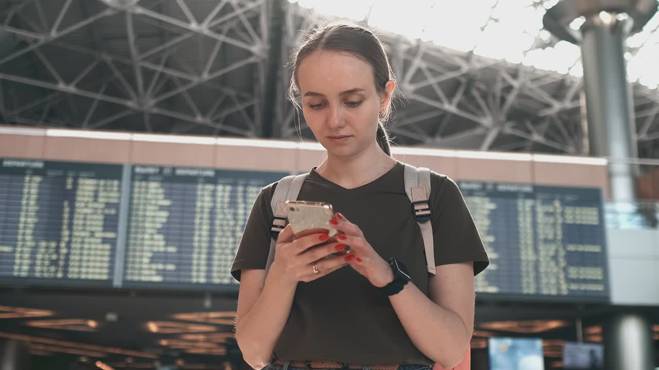 una mujer joven en el aeropuerto con un teléfono inteligente cerca de las salidas del marcador