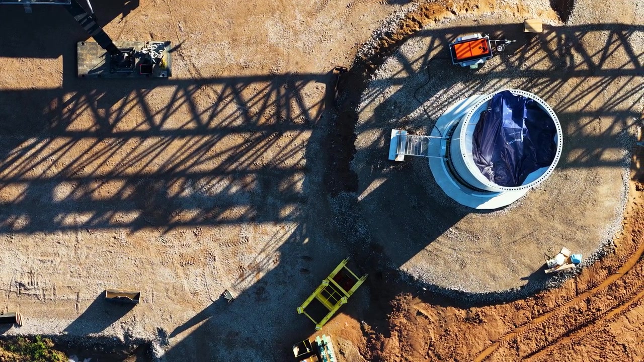 Canteiro de obras de turbina eólica mostrando a base de concreto e a sombra do guindaste