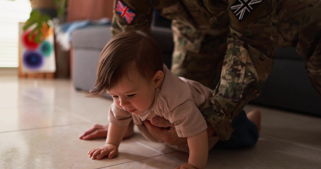Padre militare che aiuta il bambino a imparare a gattonare sul pavimento