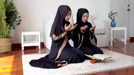 young muslim woman and female friend reading quran and praying