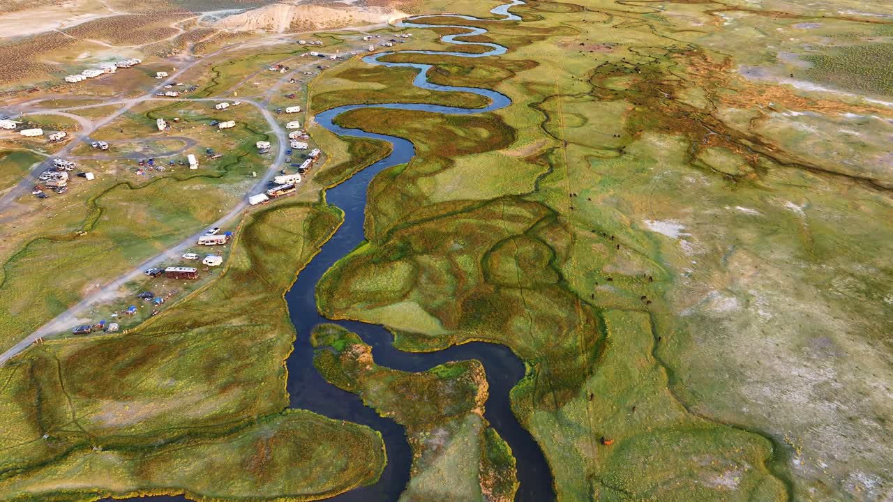 Drone above the meandering Owens River tilts up to reveal RV camping areas open meadow and distant Sierra peaks in warm daylight. Smooth reveal and graphic river curves