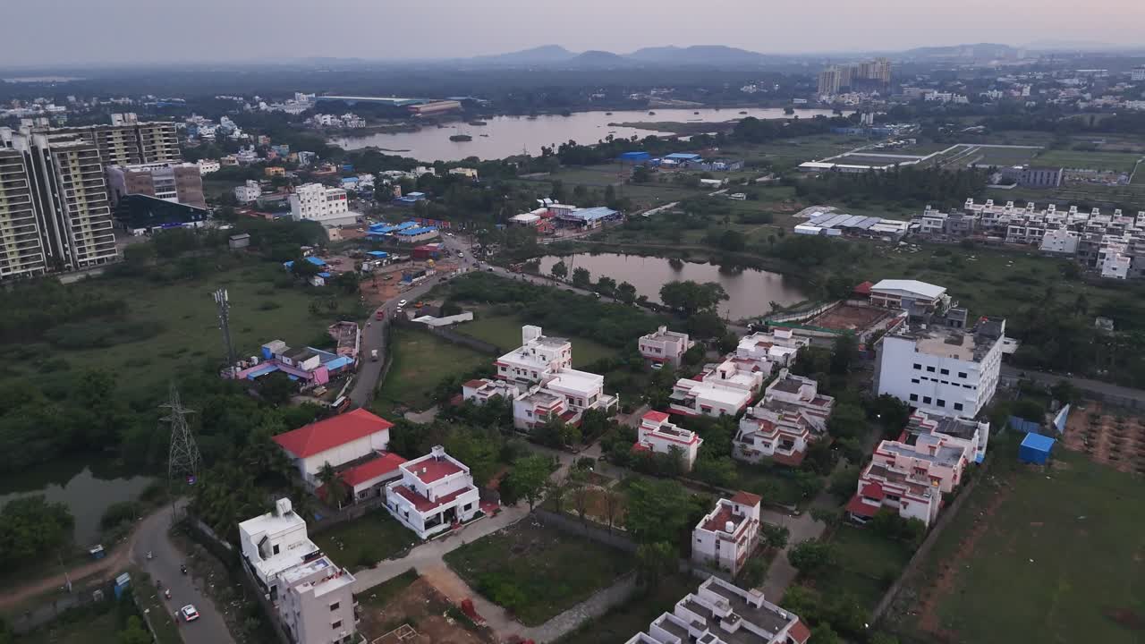 Wide-angle footage of urban expansion at dusk. The clip shows a large, placid lake framed by new residential and commercial buildings, highlighting the balance between nature and rapid city growth