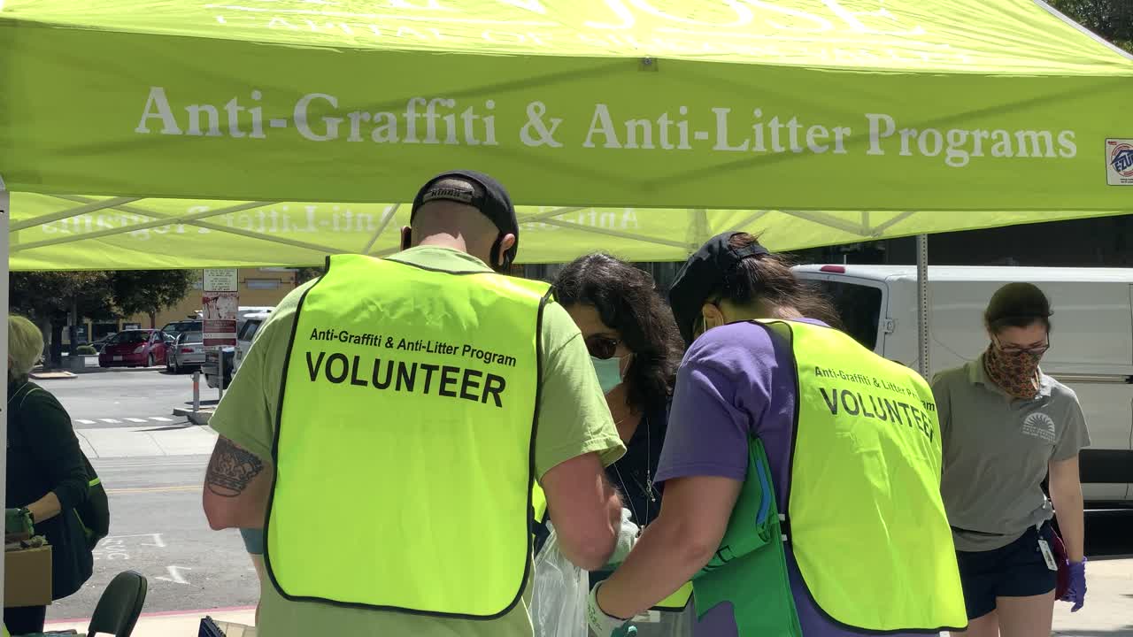Two unidentified volunteers from behind with the word "volunteer" on yellow vests, after cleaning up graffiti and litter following George Floyd protest, with sign-in booth in background