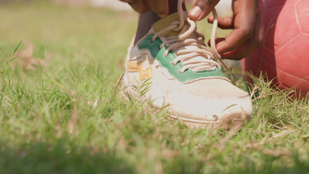 Bambino che si allaccia le scarpe accanto a un pallone luminoso. Bambino che sistema i lacci delle scarpe vicino a un pallone colorato sull'erba verde. Bambino piccolo che allaccia le scarpe accanto a un pallone vivace su un campo erboso ben curato.