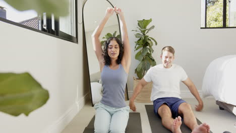 stretching together on yoga mats, young multiracial couple practicing yoga at home