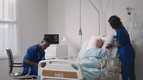 caring african ethnic medical team at the bedside of an elderly male patient. caring health care providers monitor vital signs of an elderly male hospital patient