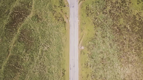 Aerial,-flying-over-a-highway-with-a-car-pulled-over-in-Dartmoor-National-Park,-UK,-tilt-shot