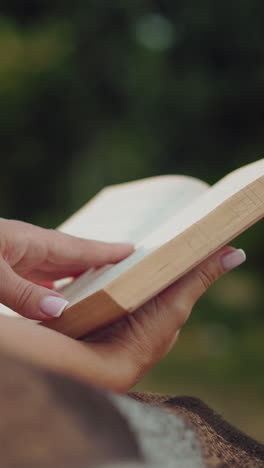 primer plano de las manos de una persona sosteniendo un libro en una manta rústica, con un fondo de vegetación suavemente borroso que hace hincapié en la tranquilidad y la inmersión en la lectura