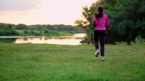 a girl in a pink jacket and black pants runs near the river in headphones preparing for the marathon