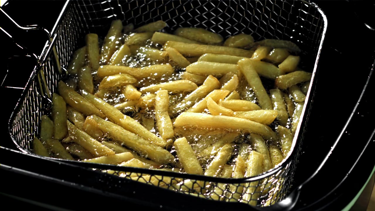 Patatine fritte dorate che friggono nell'olio bollente in una friggitrice