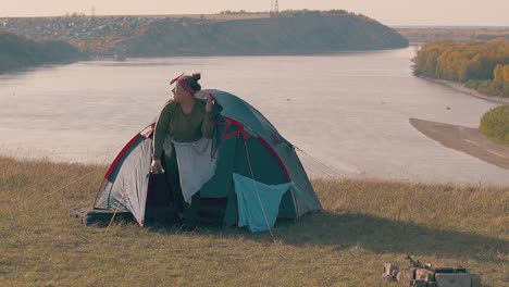 young plump woman gets out of blue tent and drinks water