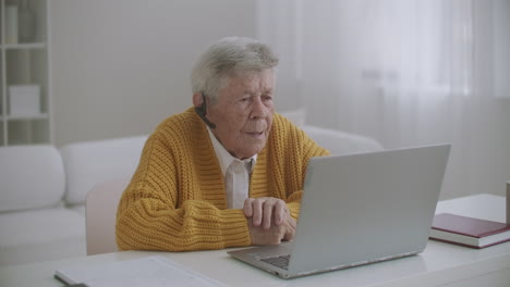 elderly-Woman-are-using-laptop-to-make-video-call-talking-gesturing-showing-thumbs-up-hand-gesture-indoors.-Old-woman-and-modern-devices-concept.