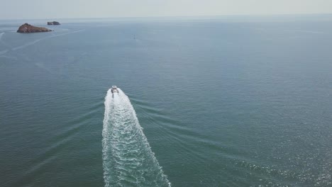 drone footage of a seafaring motorboat traveling on the surface of an ocean near the coastline