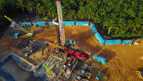 Cinematic-4K-Drone-Footage-of-Onshore-Drilling-Rig-equipment-structure-for-oil-exploration-and-exploitation-in-the-middle-of-jungle-surrounded-by-palm-oil-trees-during-sunset-and-high-oil-price