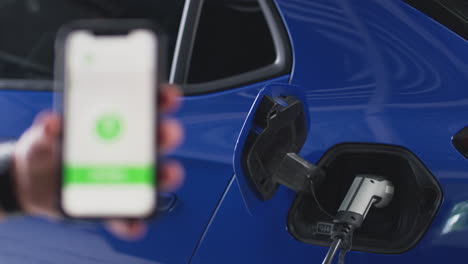 hombre cargando un coche eléctrico con cable usando una aplicación en el teléfono para monitorear el nivel de la batería