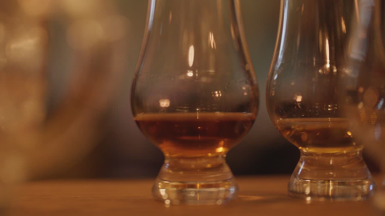 Two whisky glasses with amber liquid on wood table, softly lit by warm candlelight