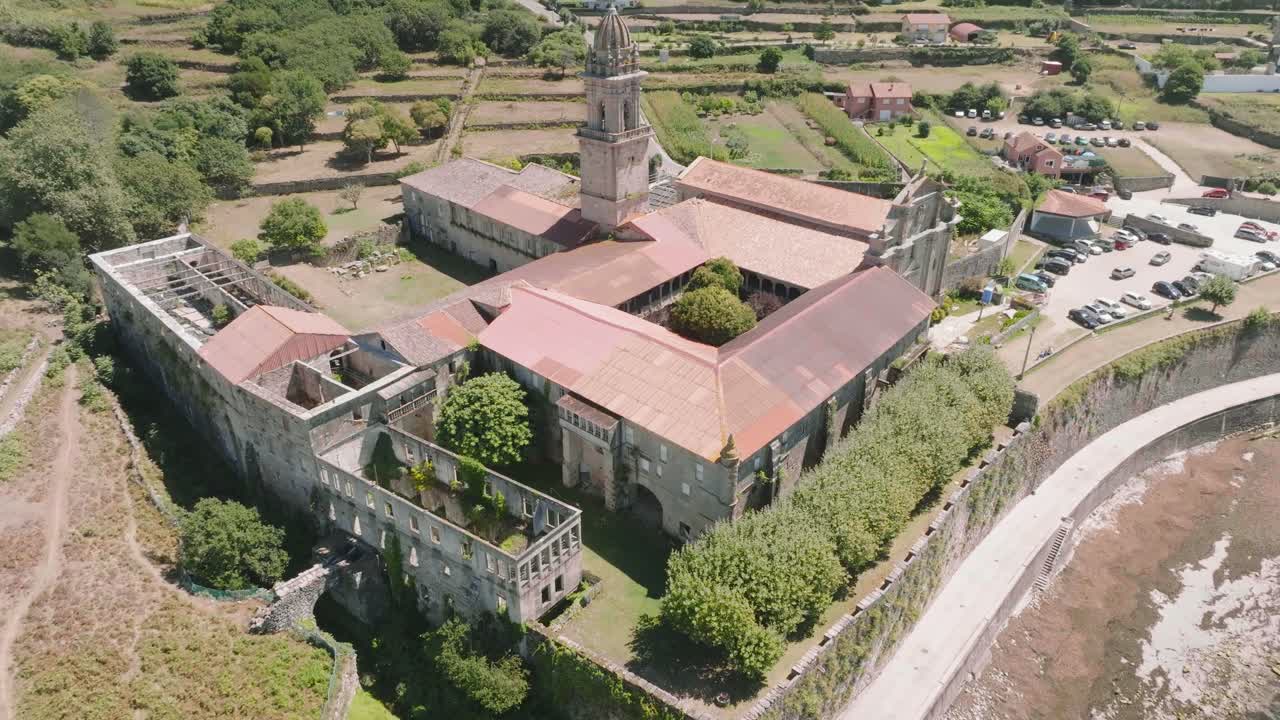 toma aérea inclinada hacia arriba de un monasterio histórico dañado ubicado en santa maria de oia con la vista de algunos autos estacionados en el fondo