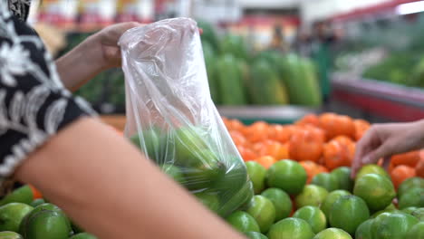 Woman's-hands-seen-selecting-limes-at-a-fresh-produce-grocery-store---isolated