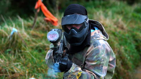 man crouching on ground shooting paintball gun