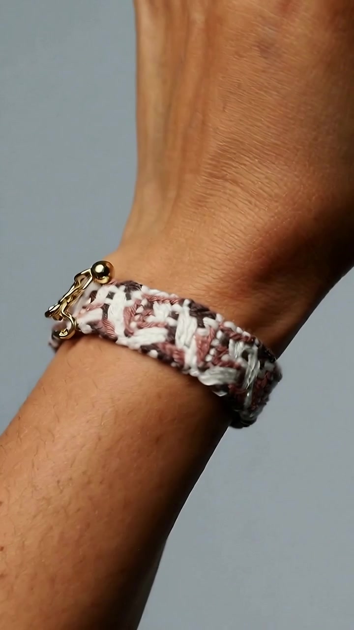 Vertical video: Flexing hand rotating adult wrist on gray backdrop, showing woven bracelet clasp