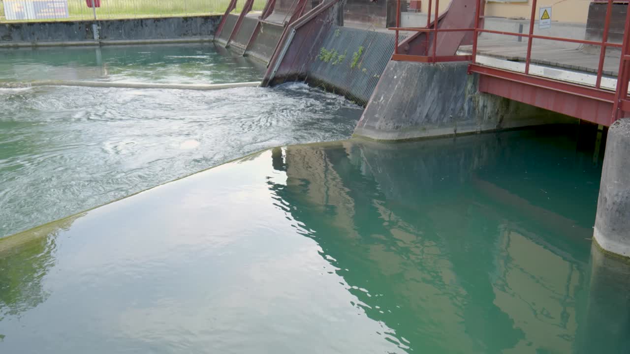 River water stream flowing in and out of a water-treatment plant dam, or a hydroelectric power plant in Switzerland, Europe. Real time, no people